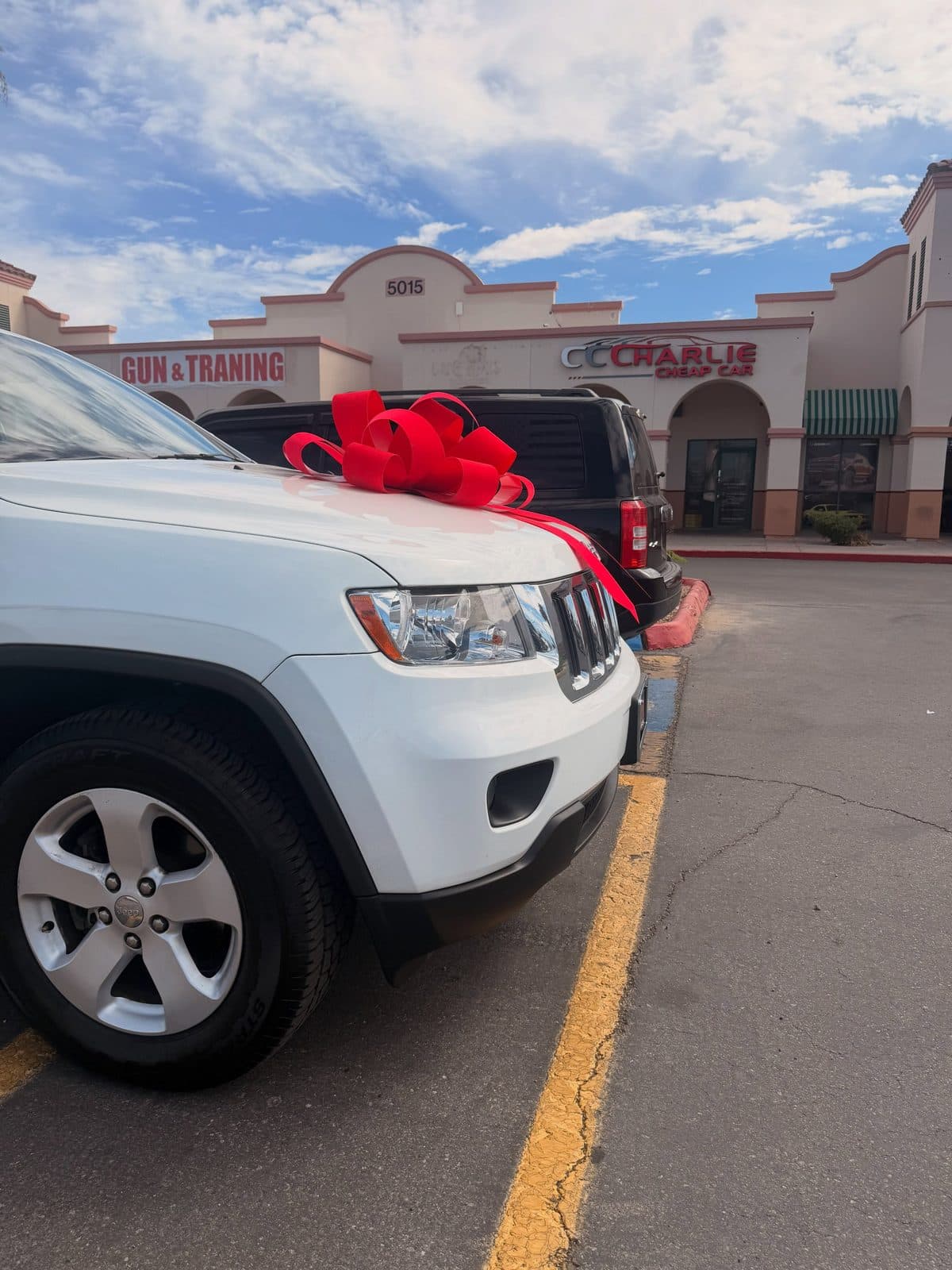 A white Jeep Grand Cherokee with a big red bow on the hood, ready for delivery at Charlie Cheap Car