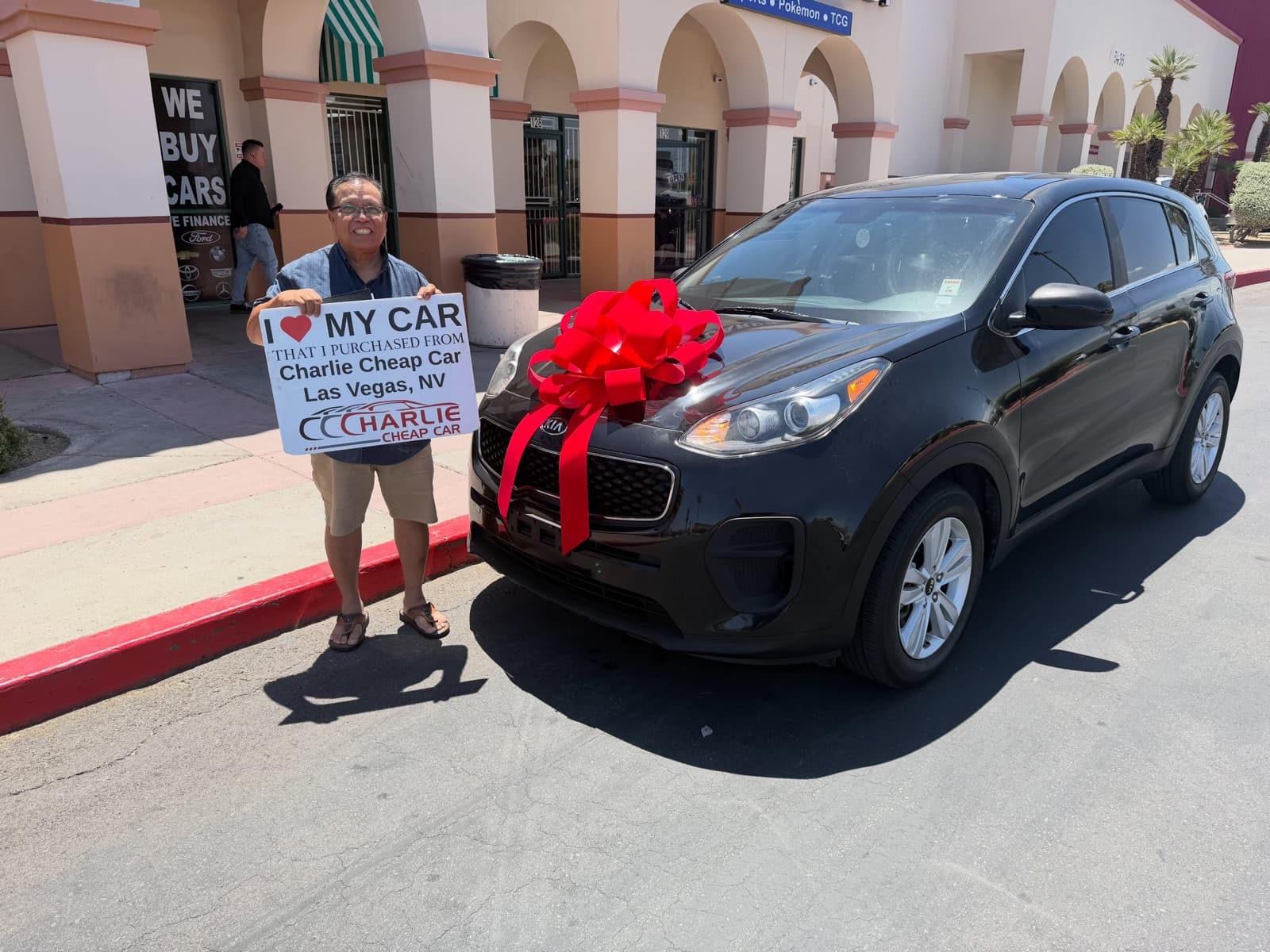 Customer holding an I love my car sign beside a black Kia Sportage with a red bow