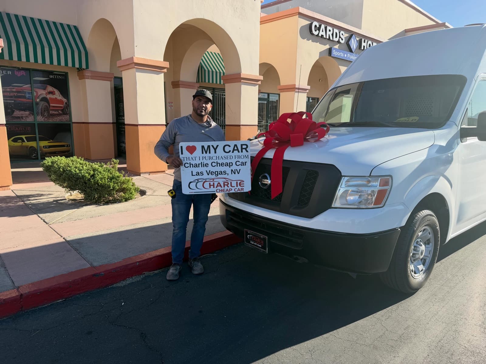 Customer with an I love my car sign next to a white Nissan NV cargo van with a red bow