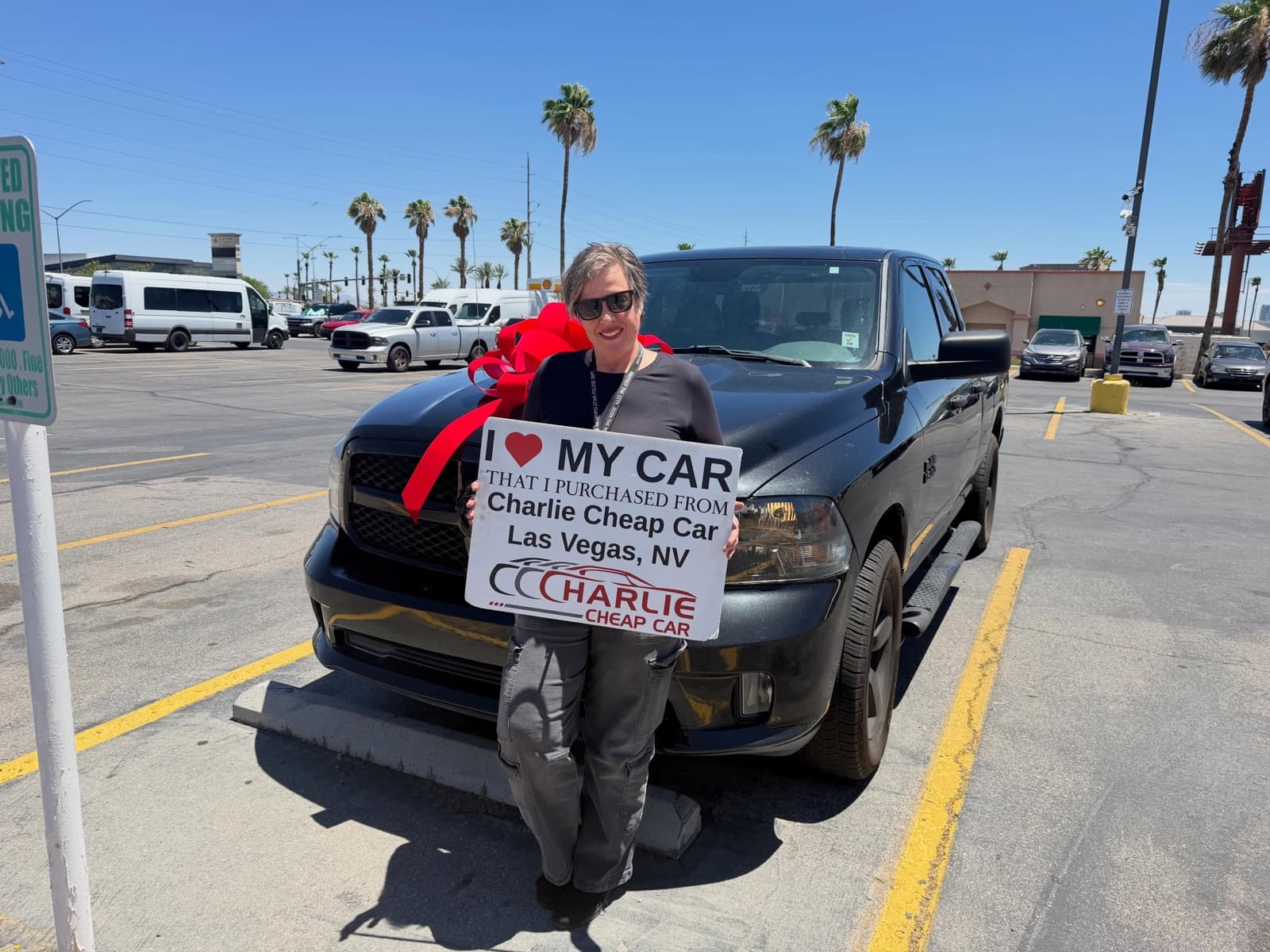 Customer holding an I love my car sign in front of a black Ram 1500 pickup with a red bow