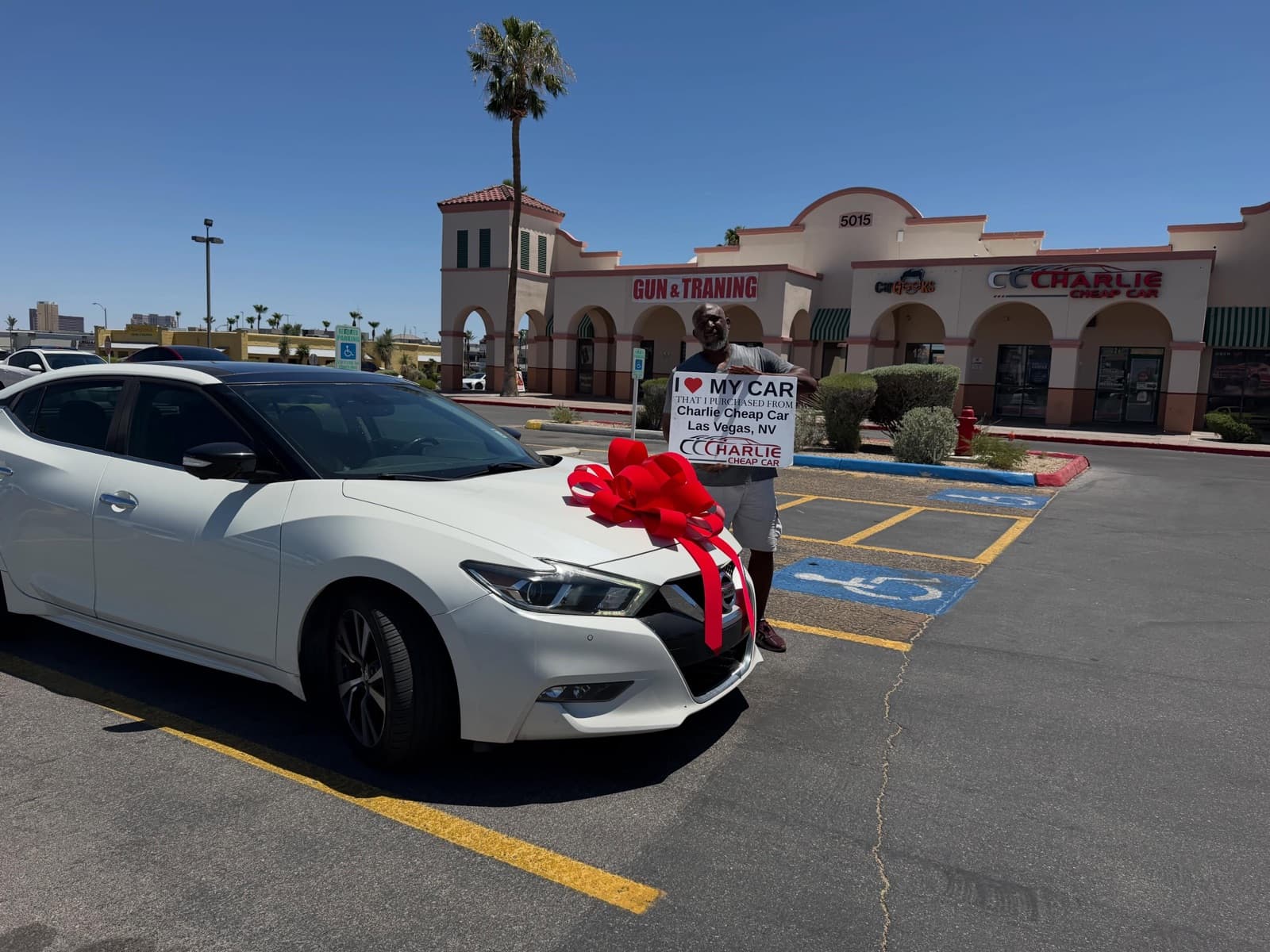 Customer holding an I love my car sign beside a white Nissan Maxima with a red bow