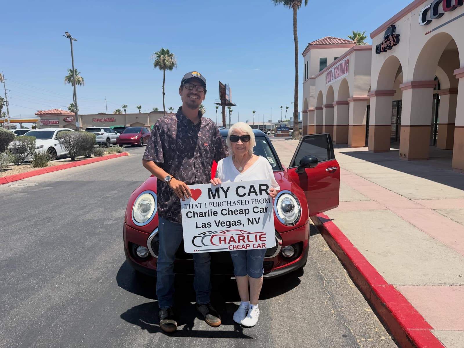 Two customers holding an I love my car sign in front of a red Mini Cooper at the dealership