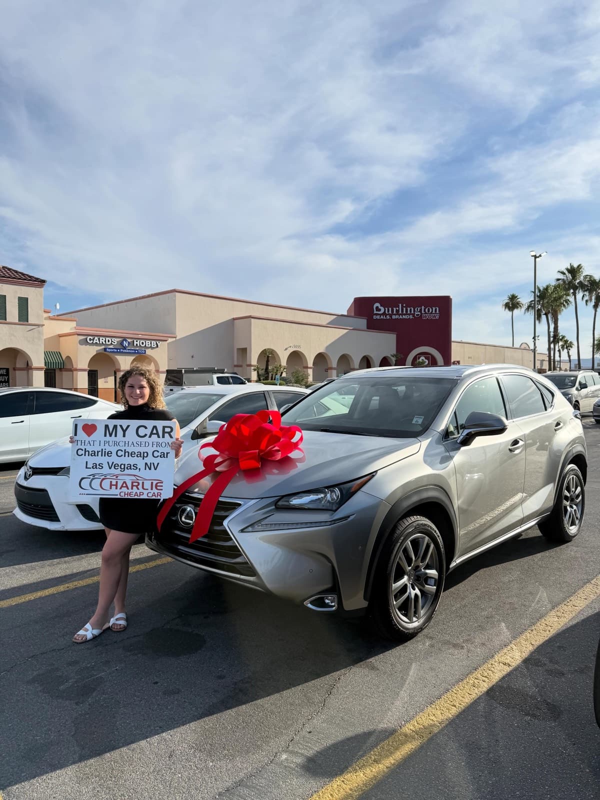 Customer holding an I love my car sign beside a silver Lexus NX SUV with a large red bow