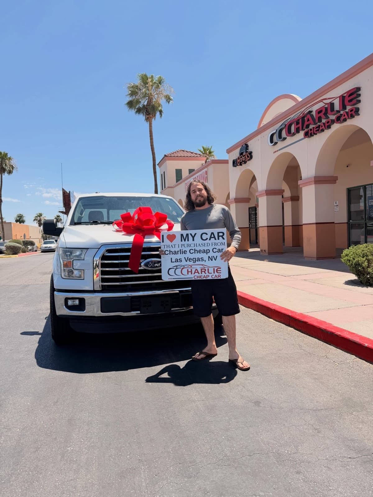 Customer holding an I love my car sign beside a white Ford F-150 pickup with a red bow