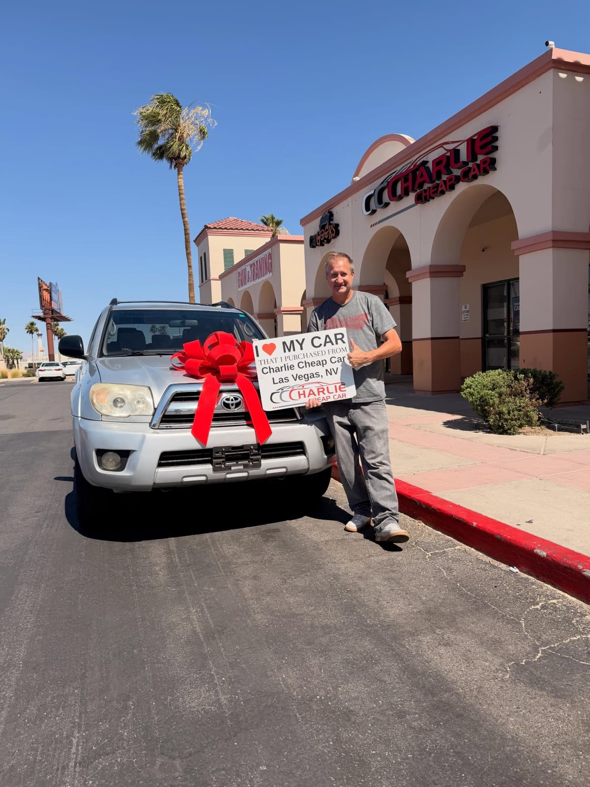 Customer with thumbs up holding the I love my car sign by a silver Toyota 4Runner with a red bow