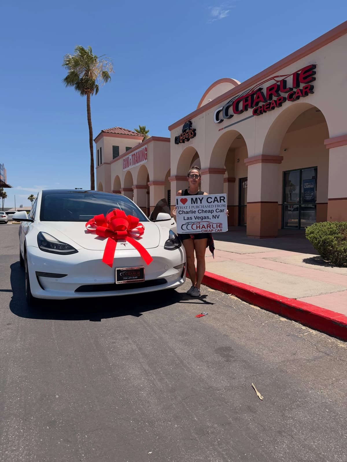 Customer holding the I love my car sign beside a white Tesla Model 3 with a red bow