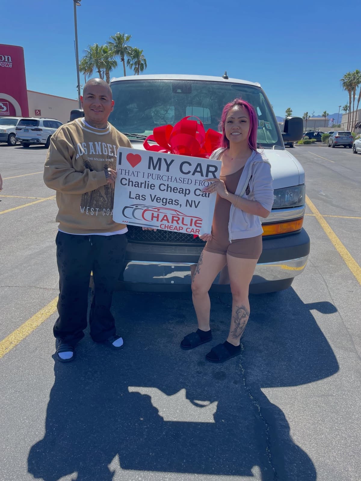 Two customers holding the I love my car sign in front of a white Chevrolet Express van